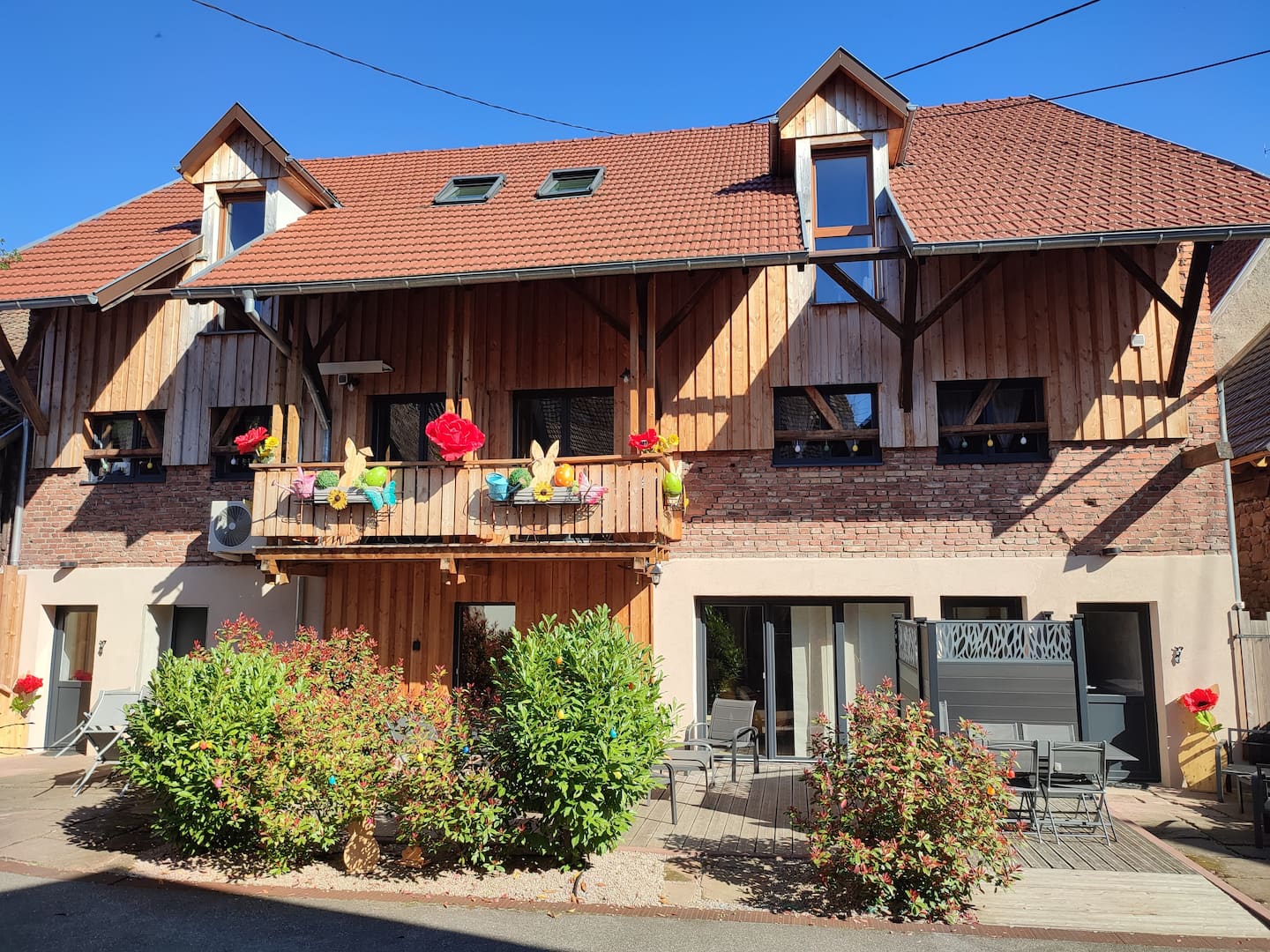 La bâtisse alsacienne restaurée des Gîtes des Prélats à Orschwiller : façade en pierre et bois, balcon fleuri et terrasses au soleil